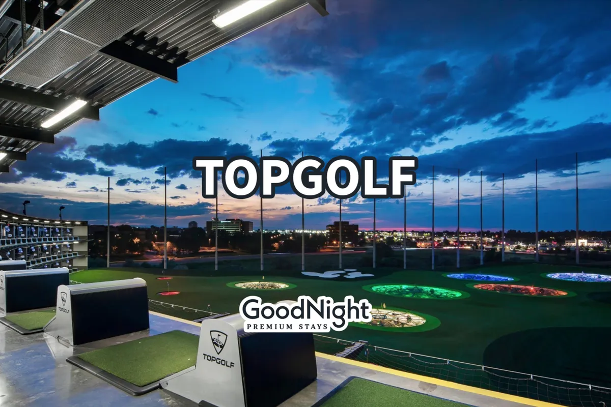 An exterior scene featuring illuminated golf bays with a dramatic skyline view in the background, captured during sunset. The setting is lively, social, and offers an elevated perspective over the city.