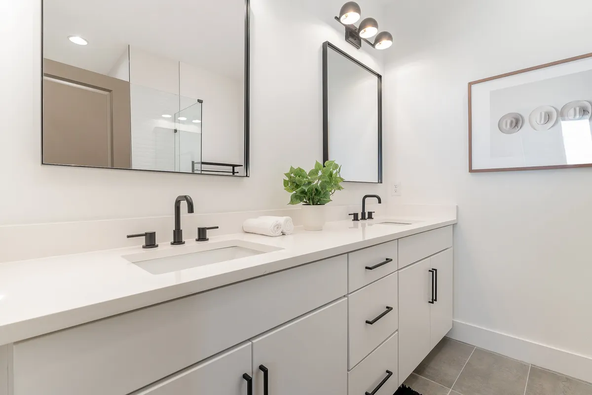 A modern bathroom featuring dual sinks with large mirrors, minimalist decor, and a touch of greenery. The room is bright, fresh, and designed for both function and relaxation.