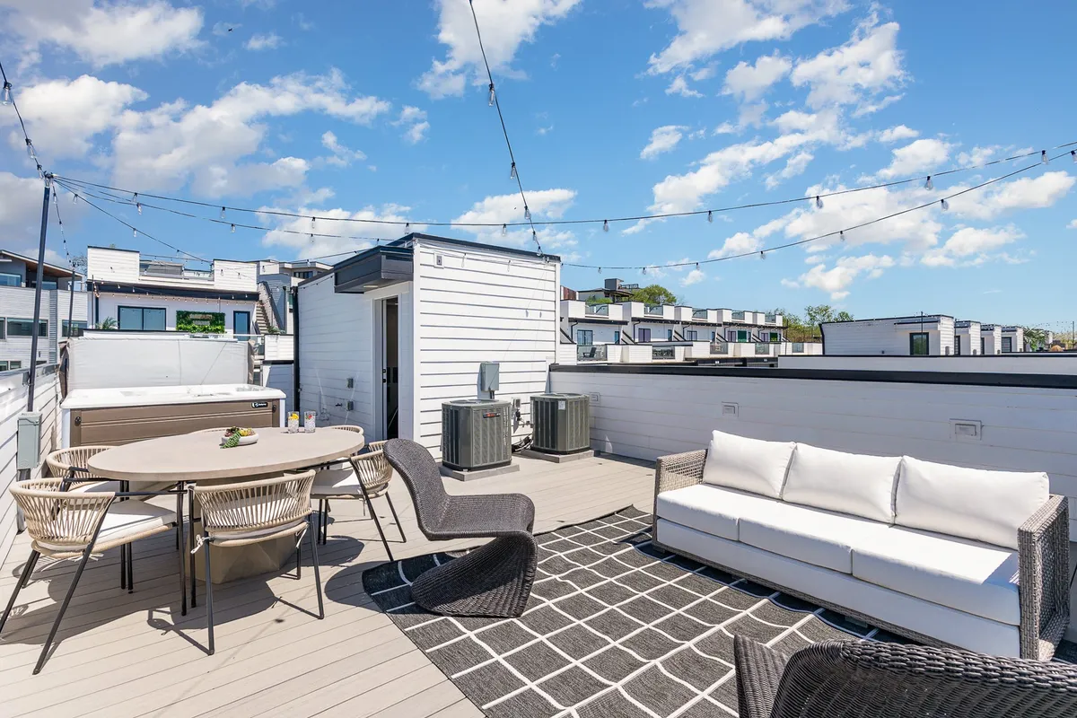 The image showcases a stylish outdoor rooftop deck with plush seating, a dining table, and a decorative rug, creating a welcoming space for guests to relax, dine, and gather. The setup encourages outdoor dining, friendly evening gatherings, and soaking in the Nashville skyline—perfect for sunset views and stargazing.