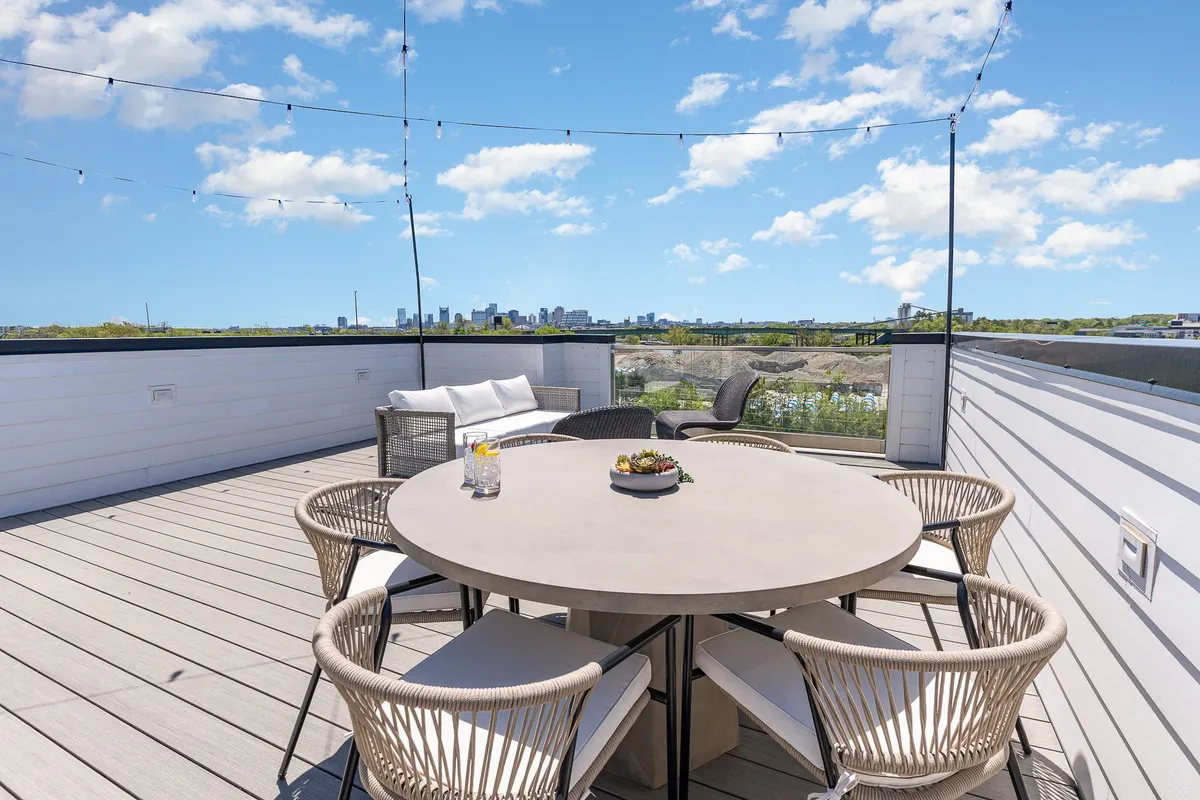 This image presents a round dining table with woven chairs on a rooftop terrace, with the Nashville city skyline in the background and soft hanging lights overhead. The mood is cheerful and relaxed, evoking the essence of rooftop celebrations and unforgettable evenings.