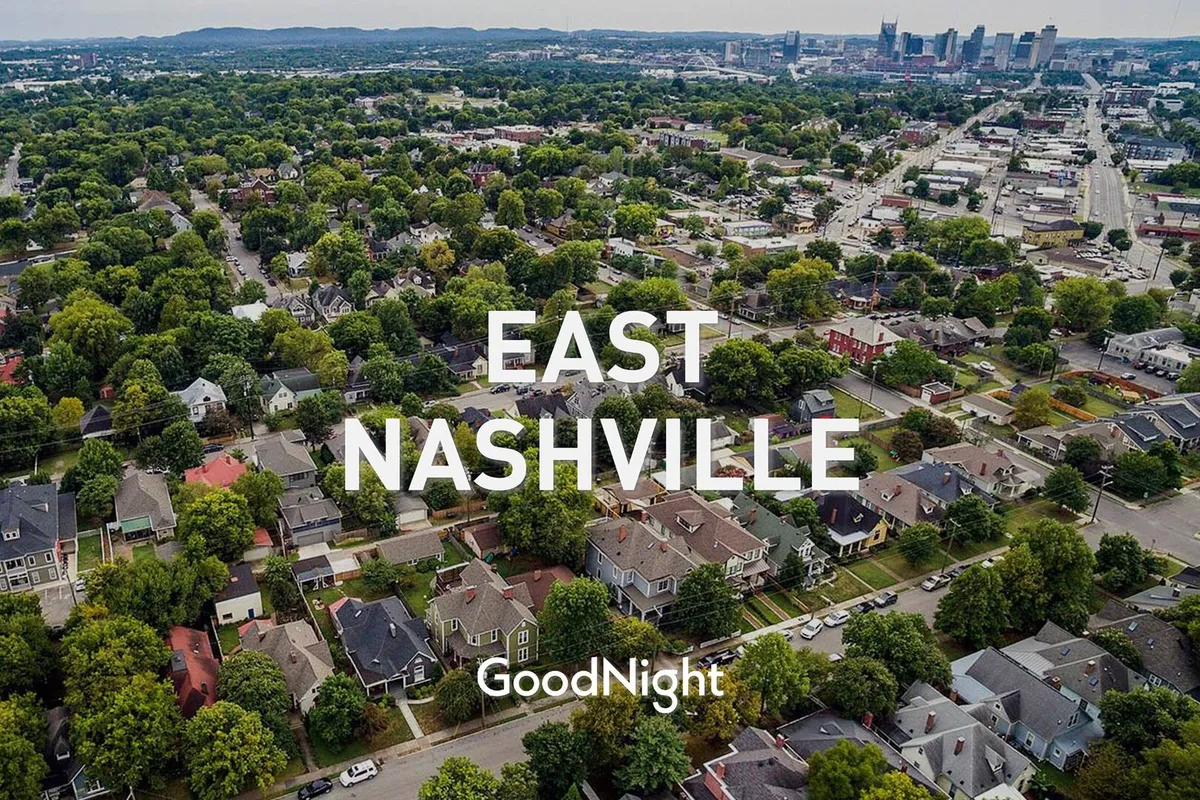 A scenic neighborhood view with residential homes surrounded by mature green trees, a distant city skyline, and people walking in a vibrant community space. The scene reflects community events, local exploration, and outdoor enjoyment.